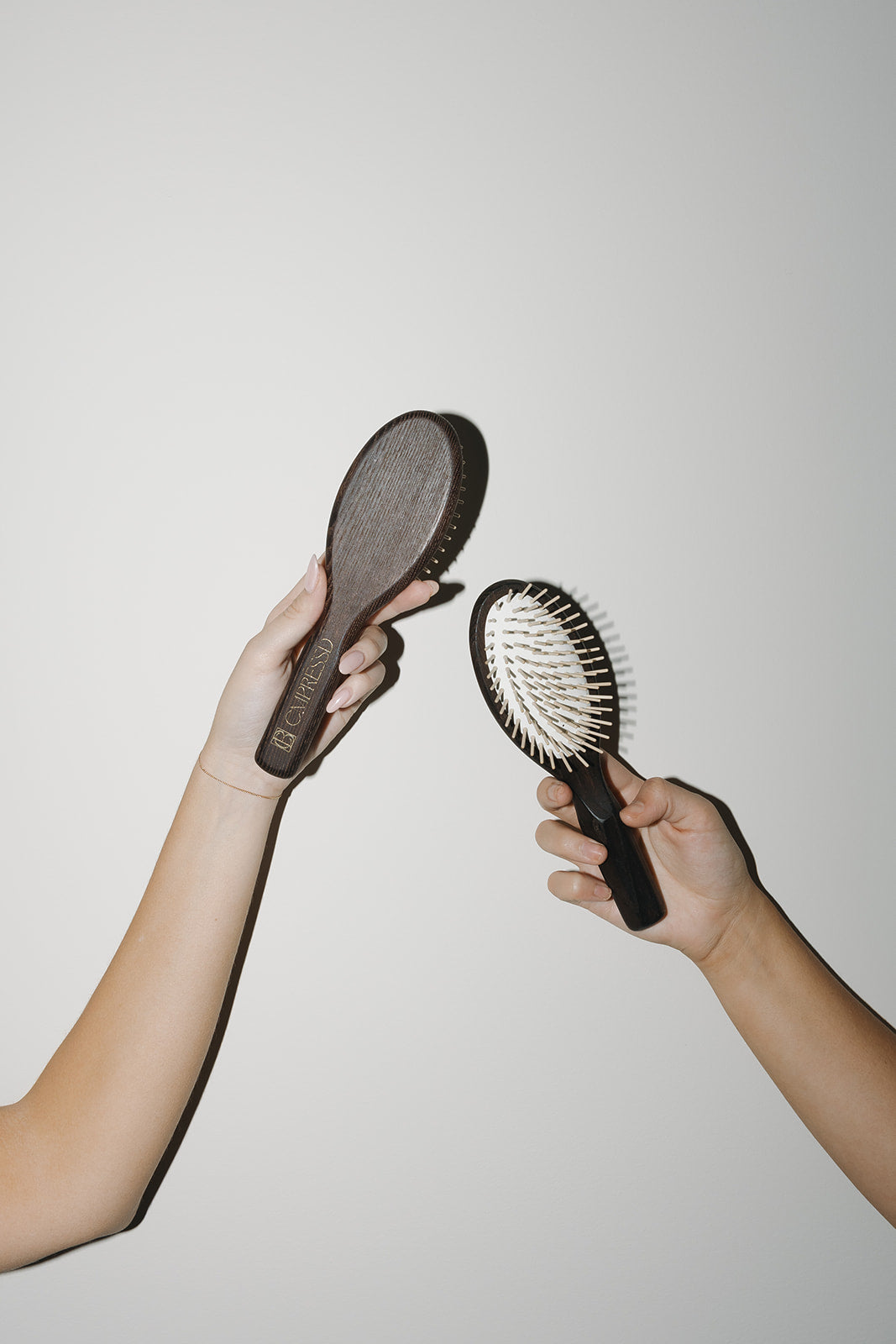 Two hands holding different hair brushes, showcasing the Dry Detangling Hair Brush and its plastic free hair care benefits.